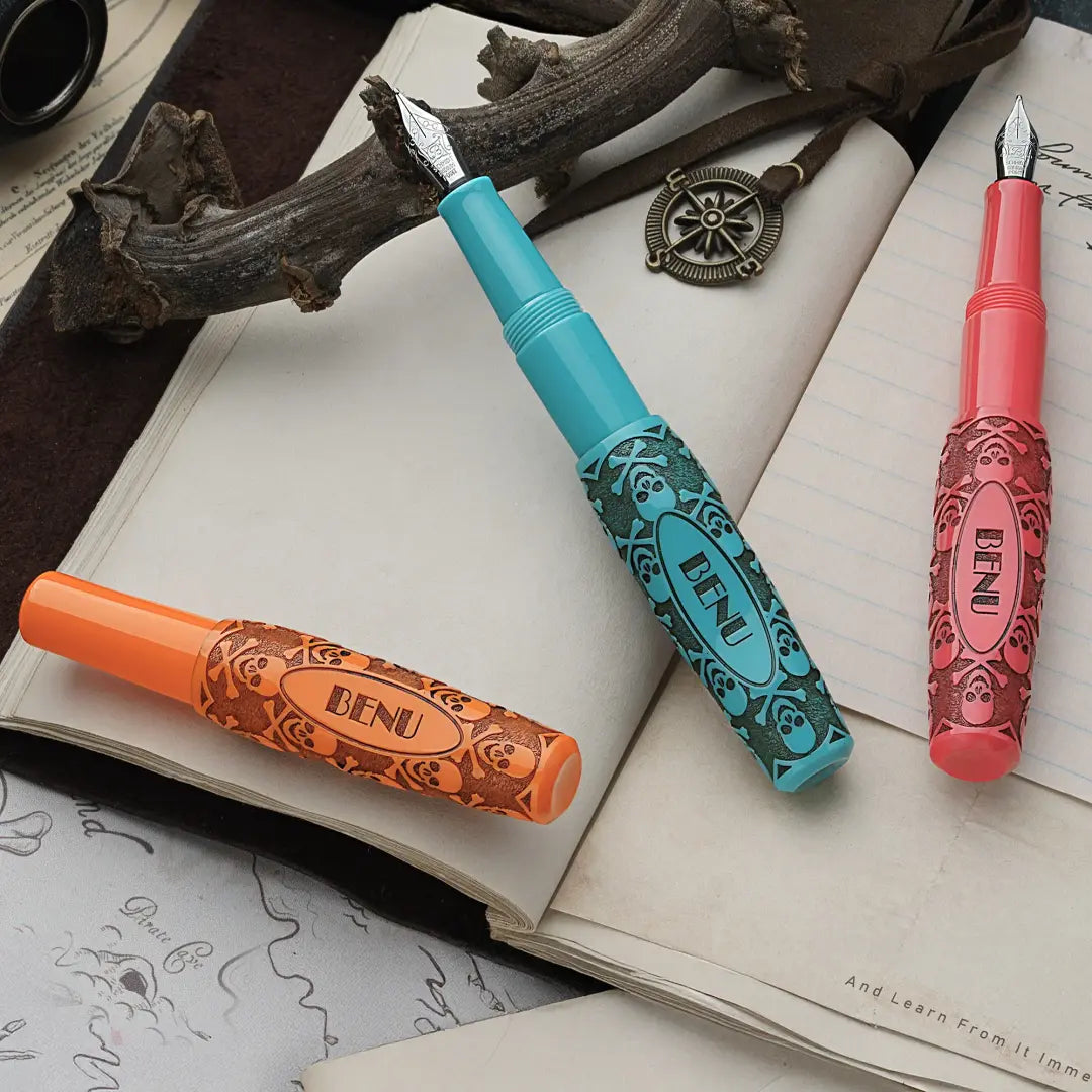 Benu Pixie Jolly Roger Vintage Füllfederhalter aus orange-pink-blauem Resin mit handaufgetragener Bitumen-Patina, antikiertem Piraten-Emblem und Schmidt-Feder