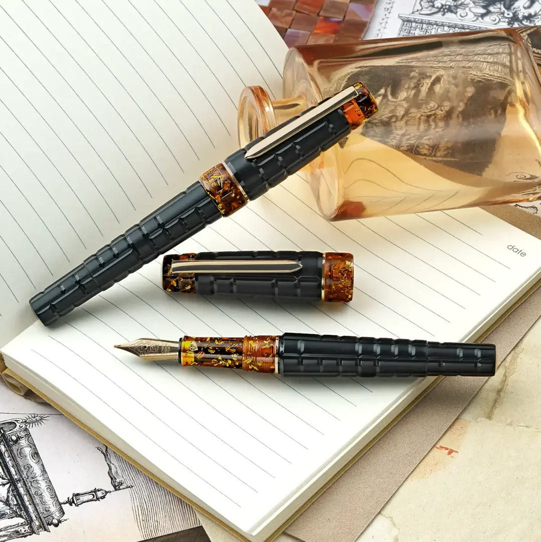 
Benu Tessera Black Amber Füllfederhalter aus mattem schwarz-ambernem Resin mit glänzenden Innenfacetten im Mosaik-Tessera-Design und vergoldetem Clip